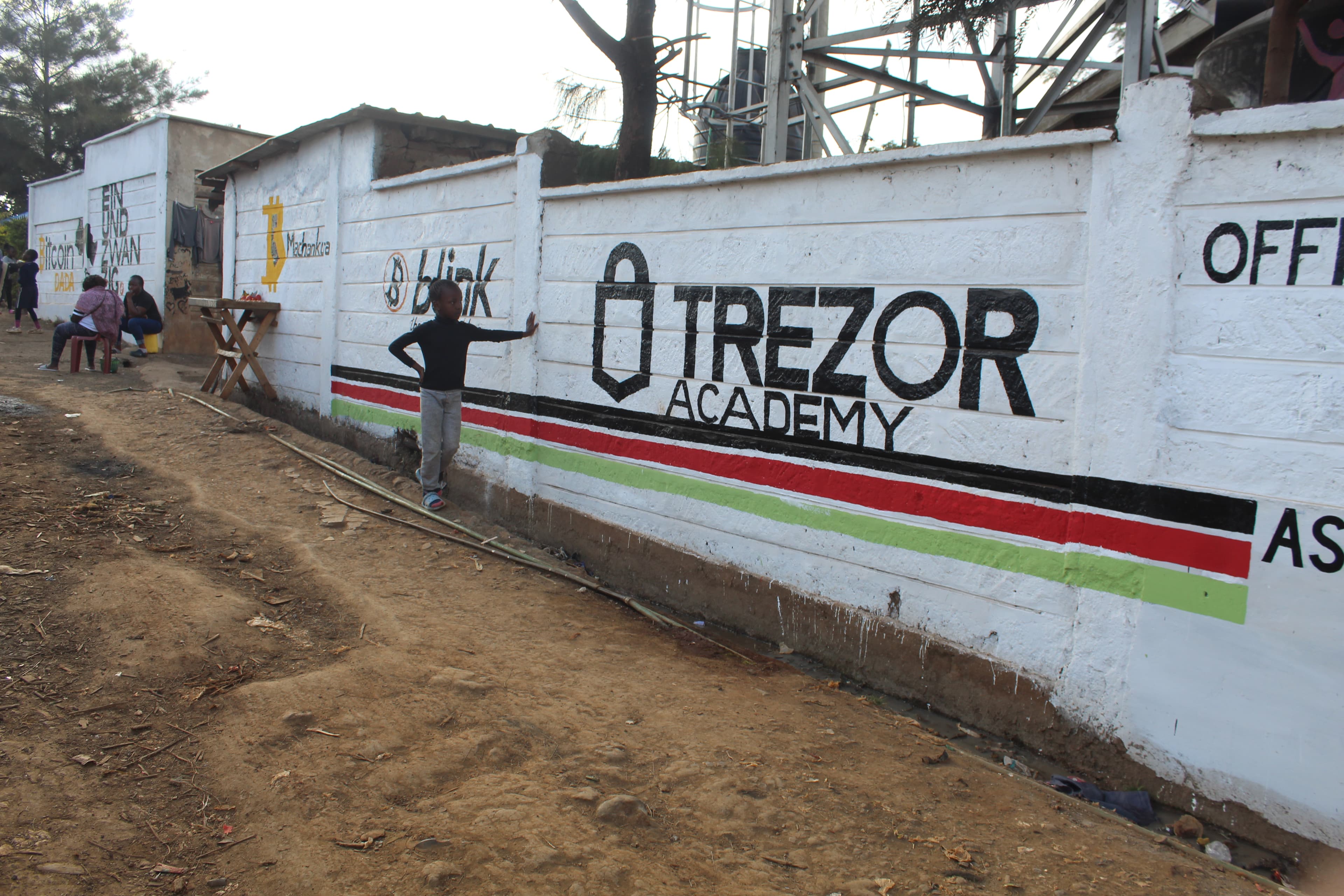 Bitcoin Dada in gold and Ein und Zwanzig in large black letters painted on a Soweto West wall, woman sitting in front