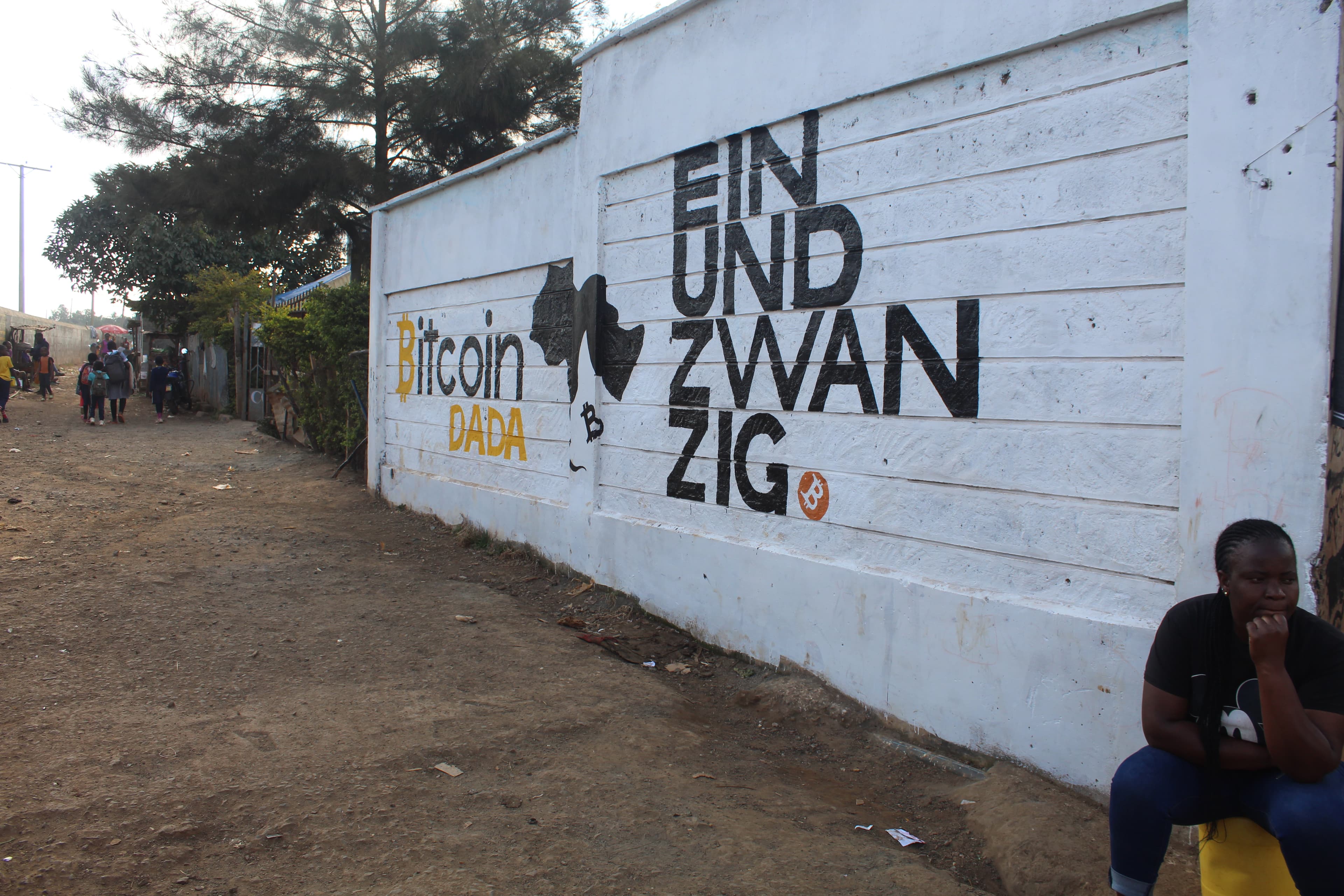 Blink and Trezor Academy logos on a long white Soweto West wall with Kenyan flag stripes, a child standing in front pointing at the Blink logo