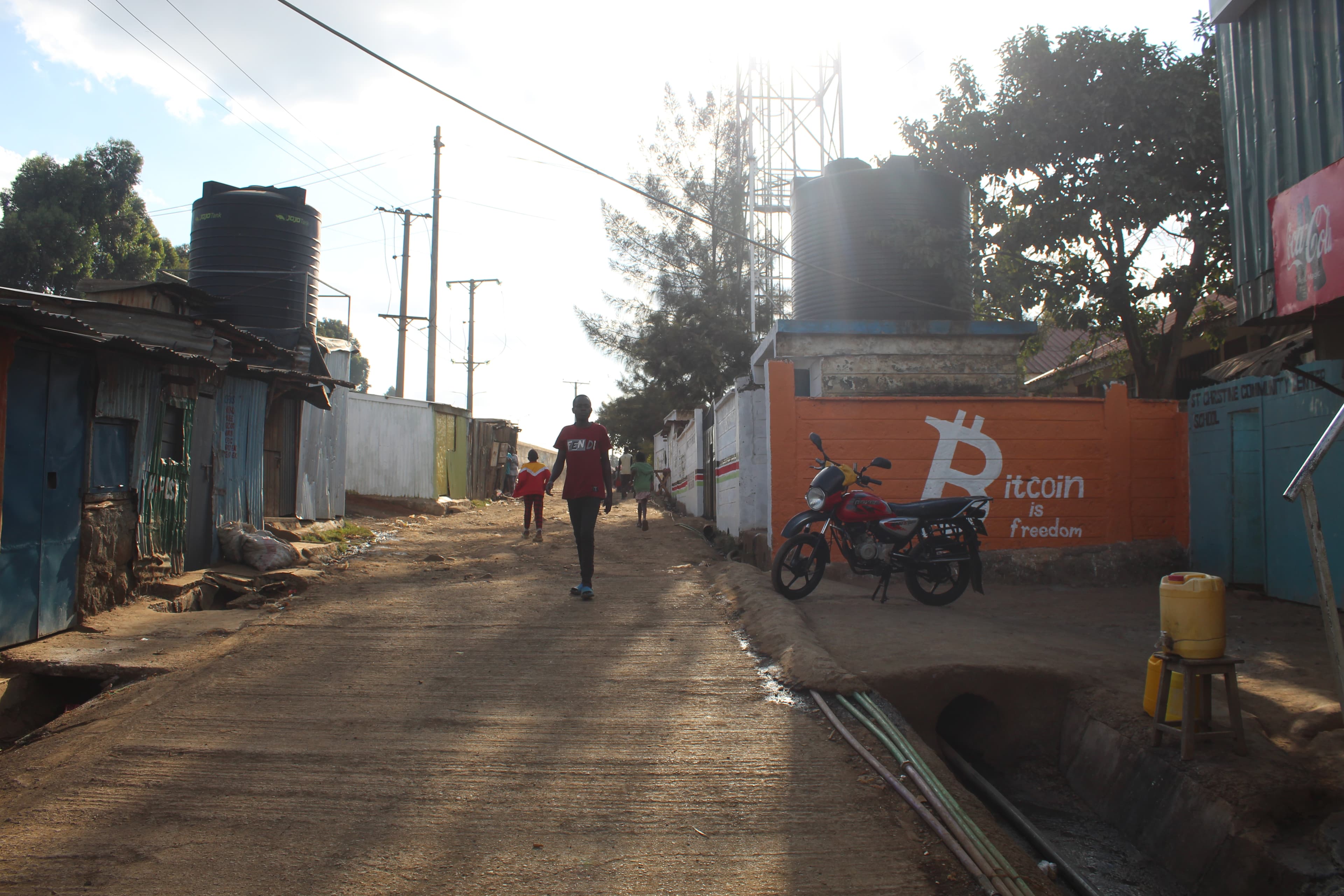 A Soweto West street with the orange Bitcoin is freedom mural on the right and a boda-boda parked in front
